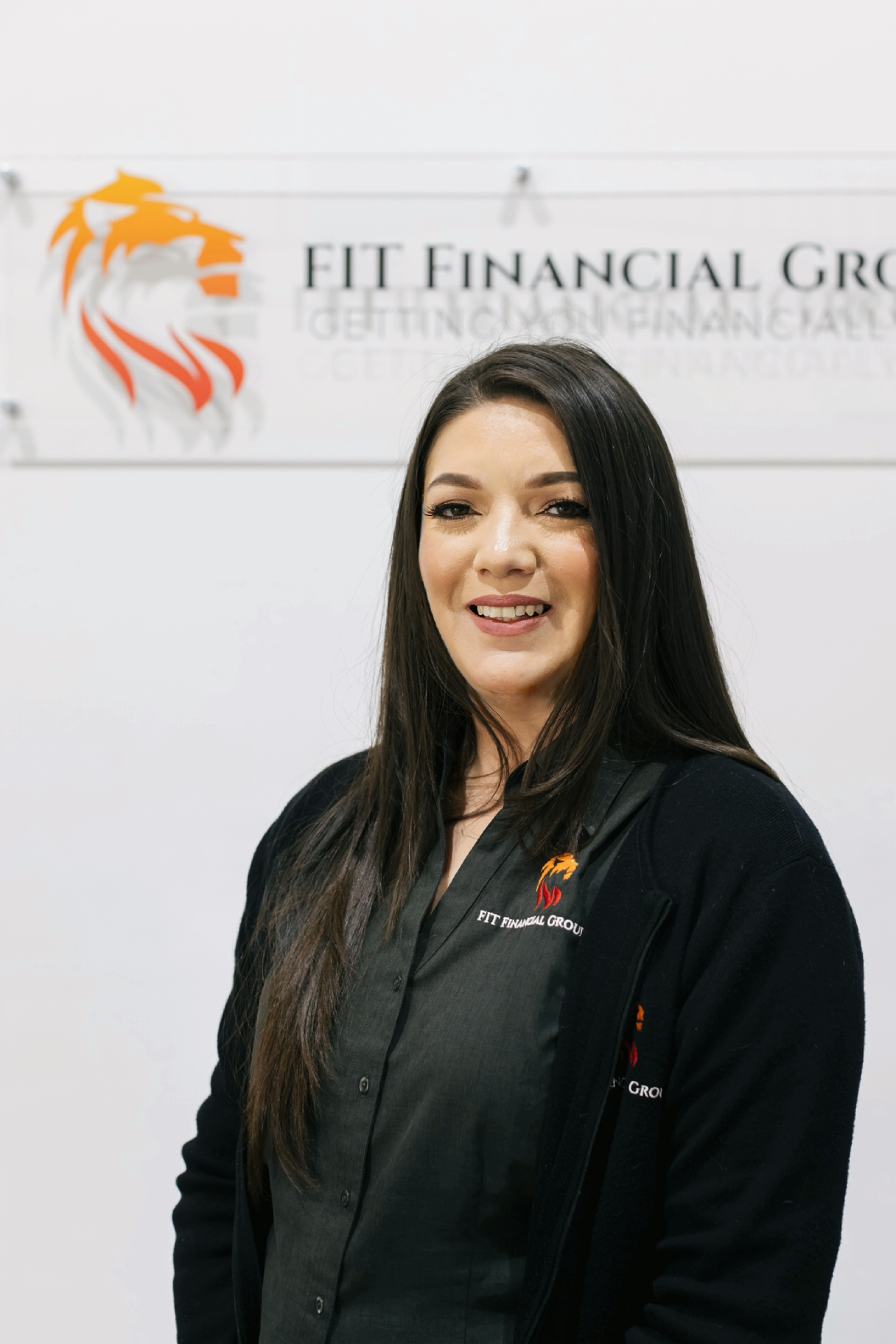 Woman in a black shirt smiles in front of a sign that says 