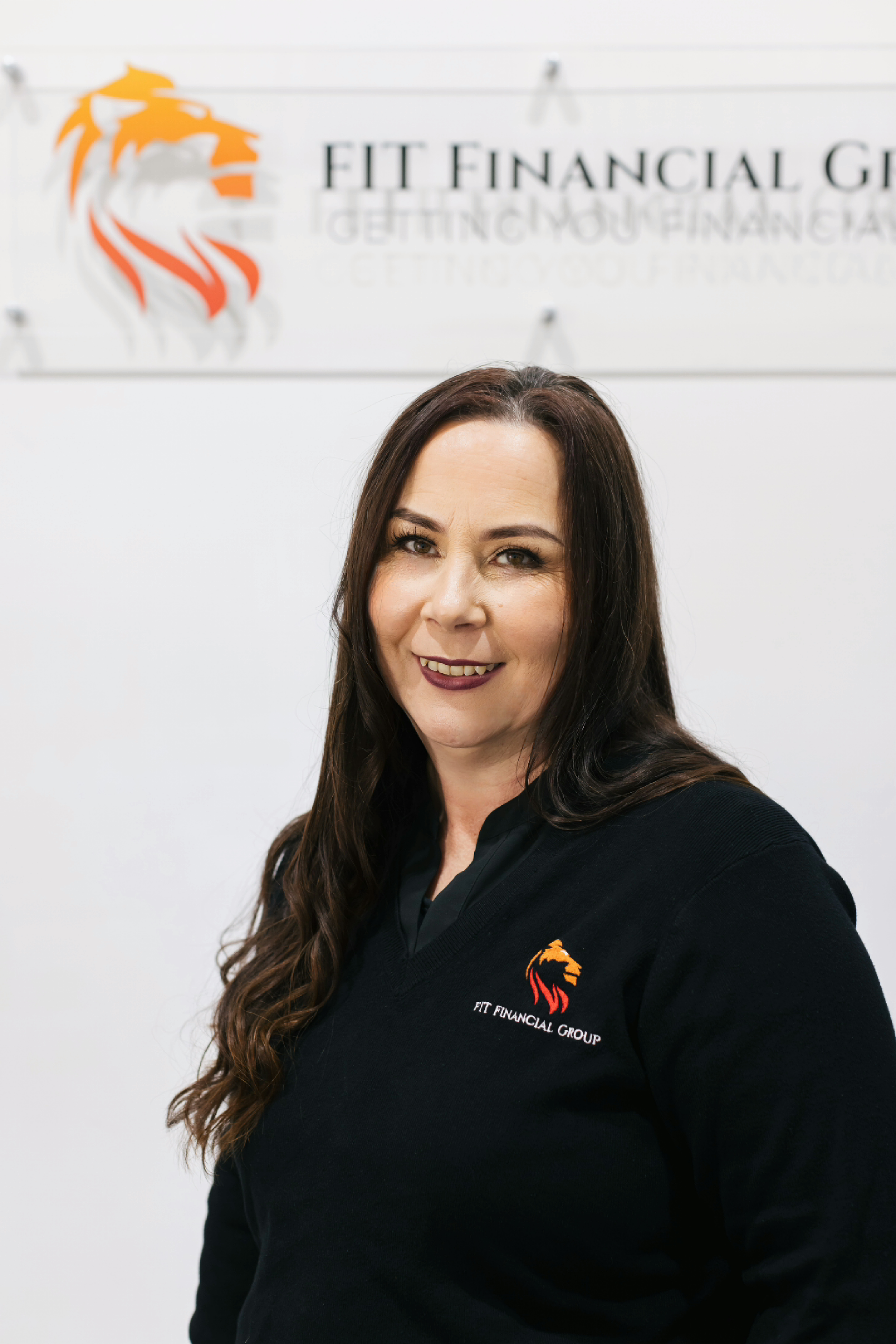 Woman in black shirt smiles in front of a sign for FIT Financial Group — Fit Financial Group in Leumeah, NSW