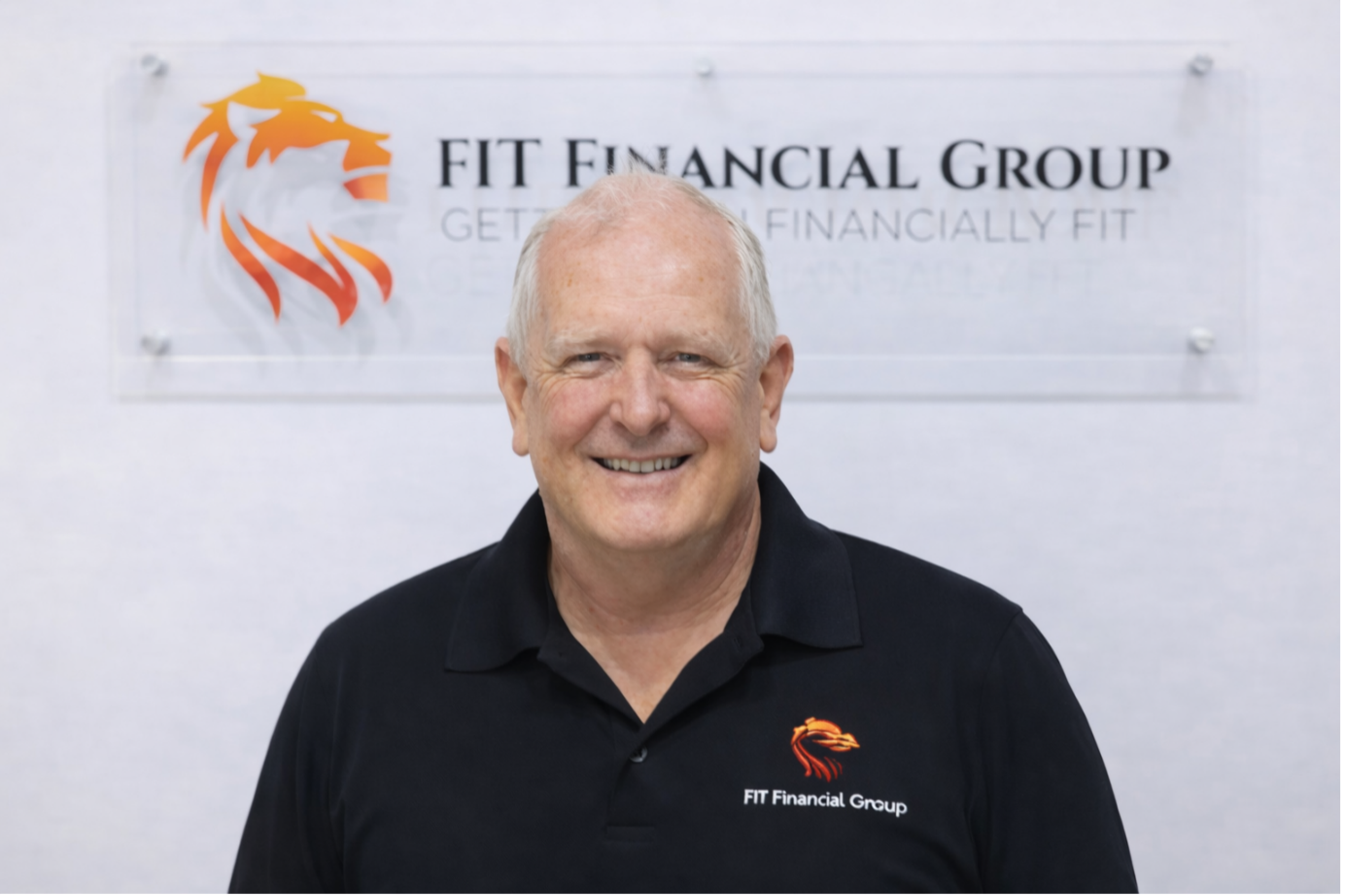 Man smiling in front of a sign for FIT Financial Group with a lion logo on a white wall — Fit Financial Group in Leumeah, NSW