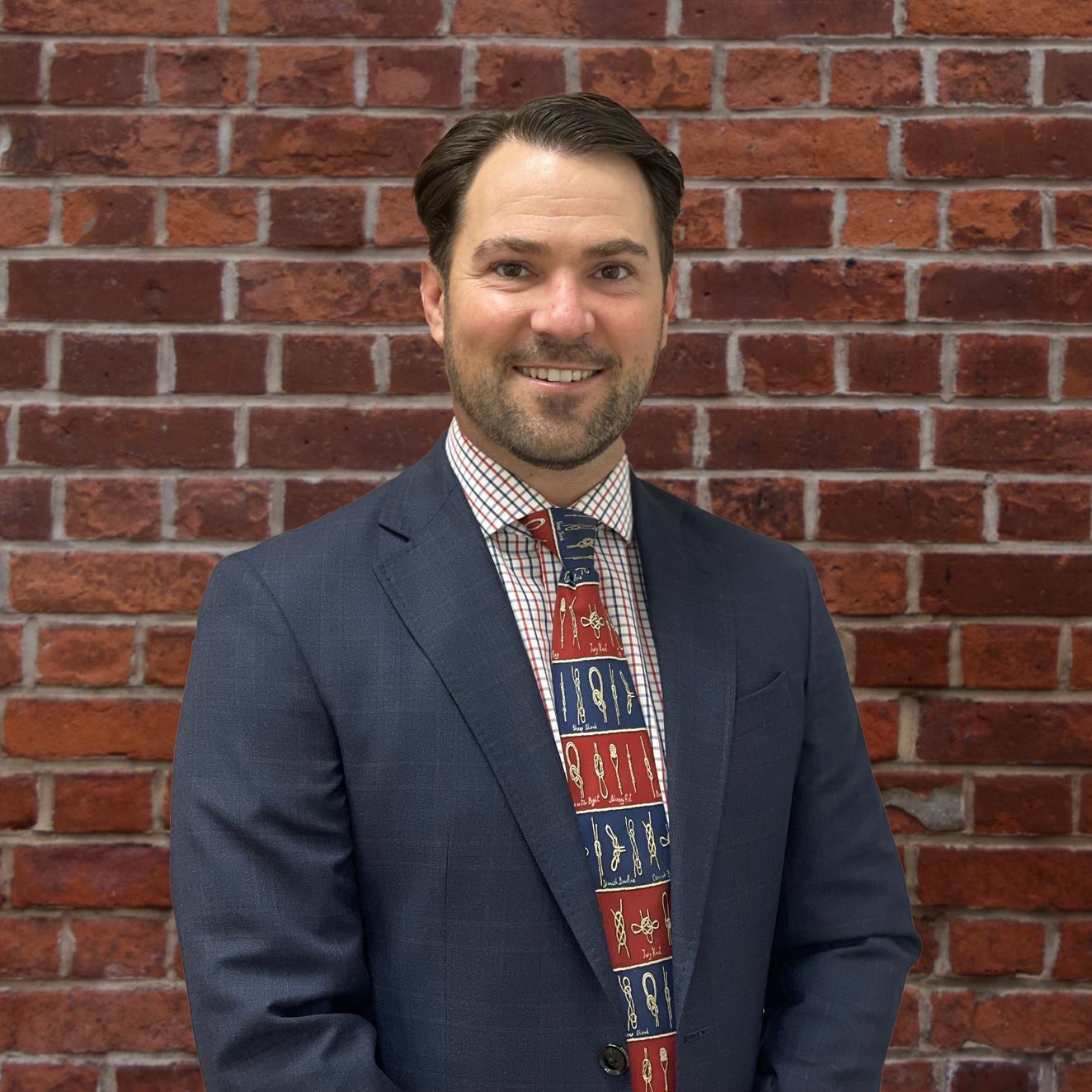 A man in a suit and tie is standing in front of a brick wall.