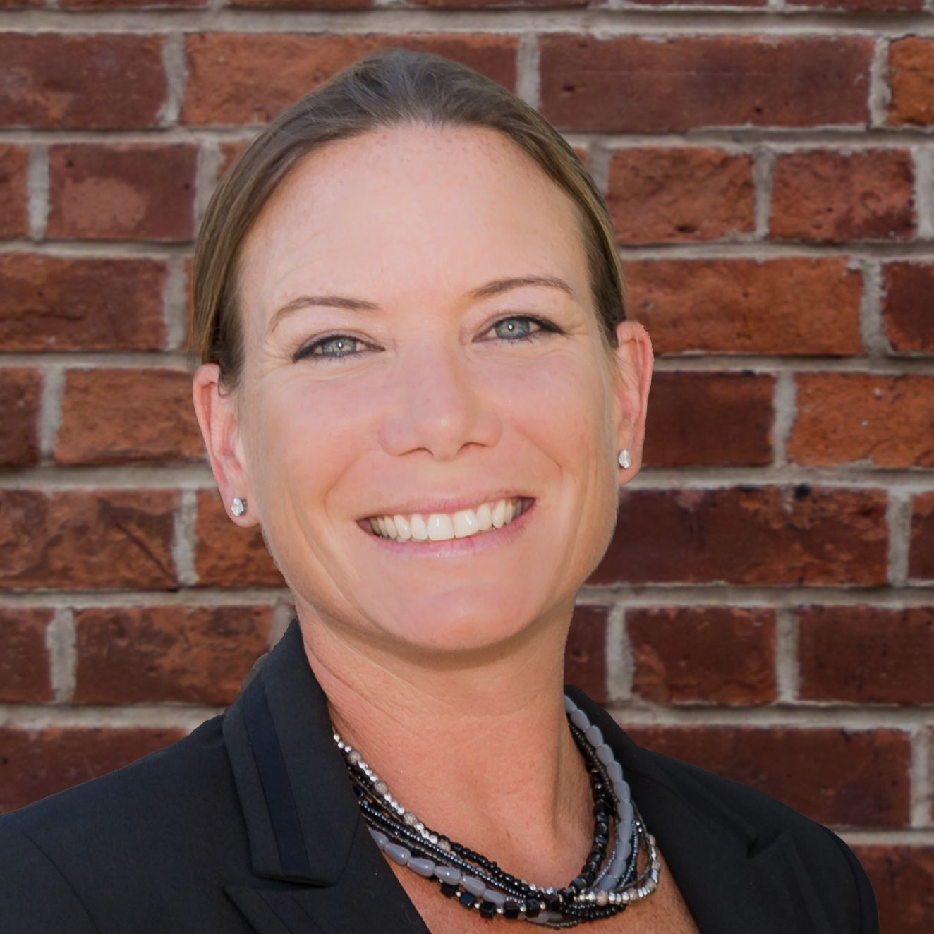 A woman is smiling in front of a brick wall