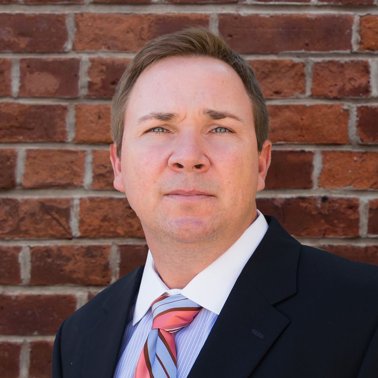 A man in a suit and tie stands in front of a brick wall