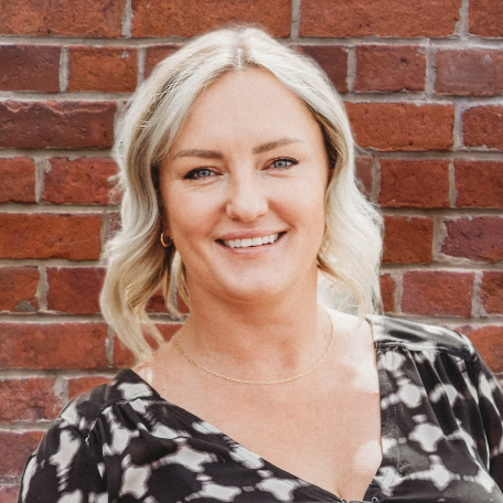 A woman is smiling in front of a brick wall