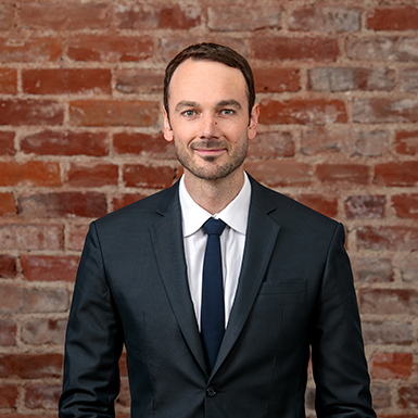 A man in a suit and tie is standing in front of a brick wall.