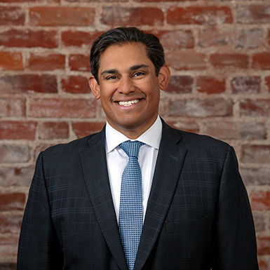 A man in a suit and tie is smiling in front of a brick wall.
