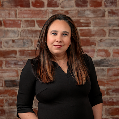 A woman in a black dress is standing in front of a brick wall.