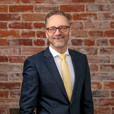A man in a suit and tie is standing in front of a brick wall.