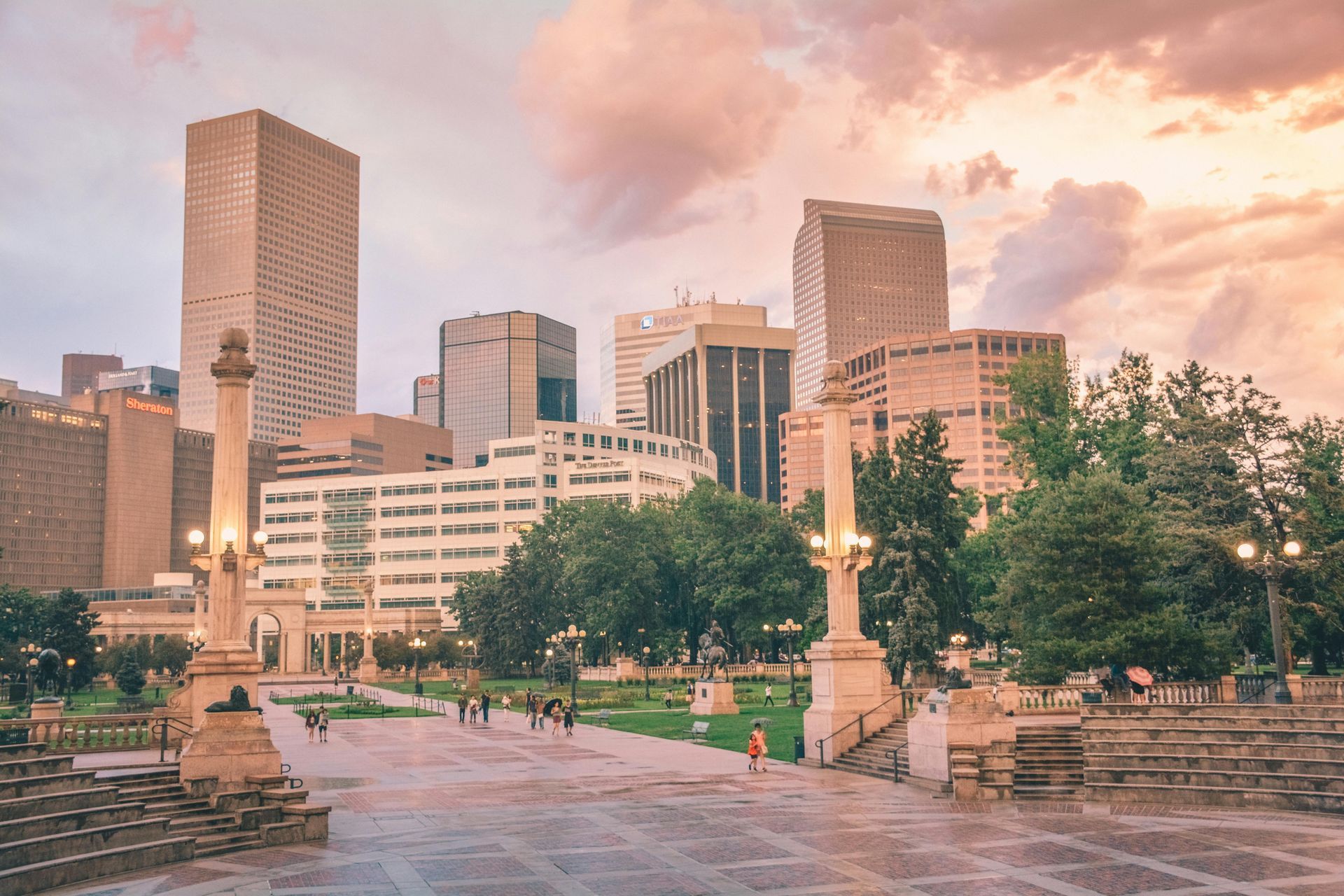 A city park with a statue in the foreground and a city skyline in the background.