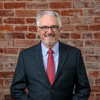 A man in a suit and tie is standing in front of a brick wall.