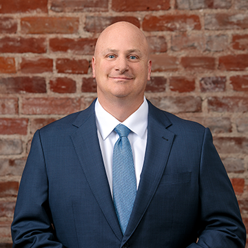 A man in a suit and tie is standing in front of a brick wall.