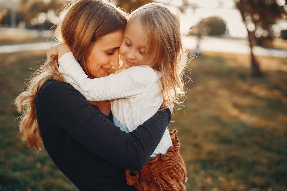 A woman is holding a little girl in her arms in a park.