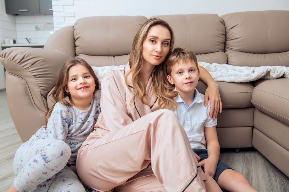 A woman and two children are sitting on the floor in front of a couch.