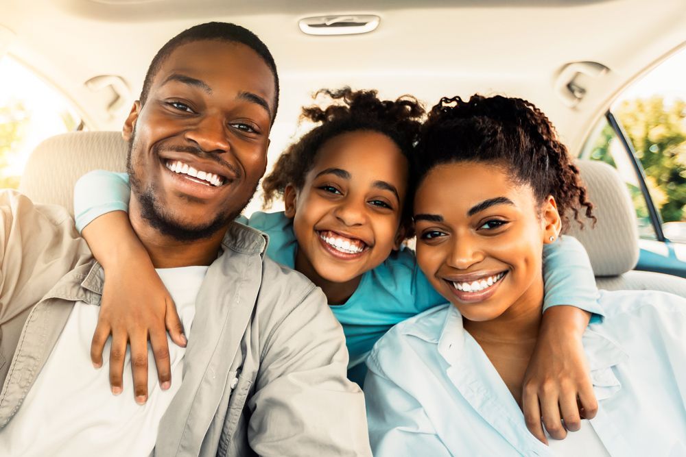 A family is sitting in the back seat of a car and smiling.