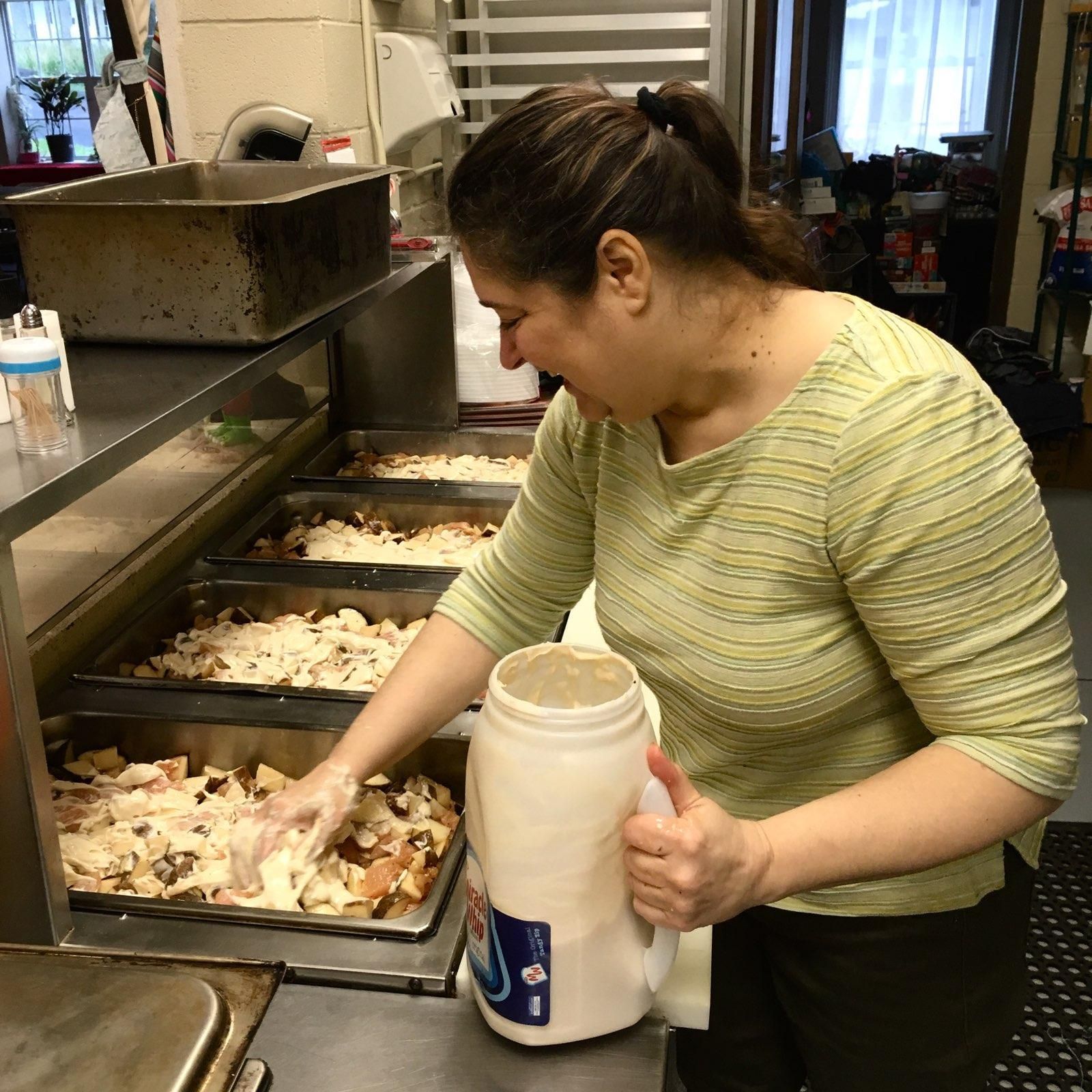 A woman in a green striped shirt is holding a white container with a blue label on it