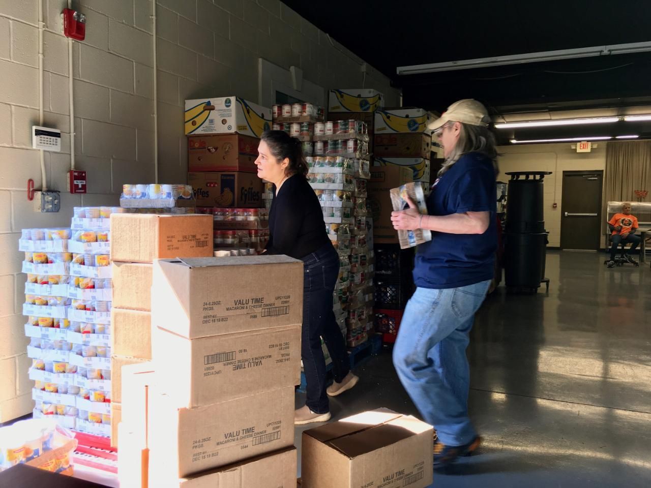 A man and a woman are moving boxes in a warehouse.
