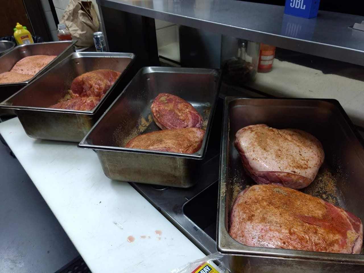 Trays of meat are lined up on a counter in a kitchen