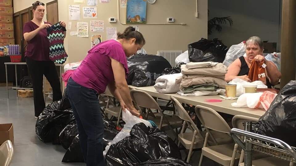 A woman is standing next to a pile of trash bags in a room.