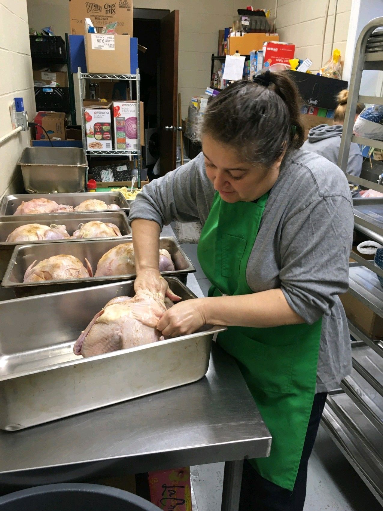 A woman in a green apron is preparing turkeys in a kitchen.