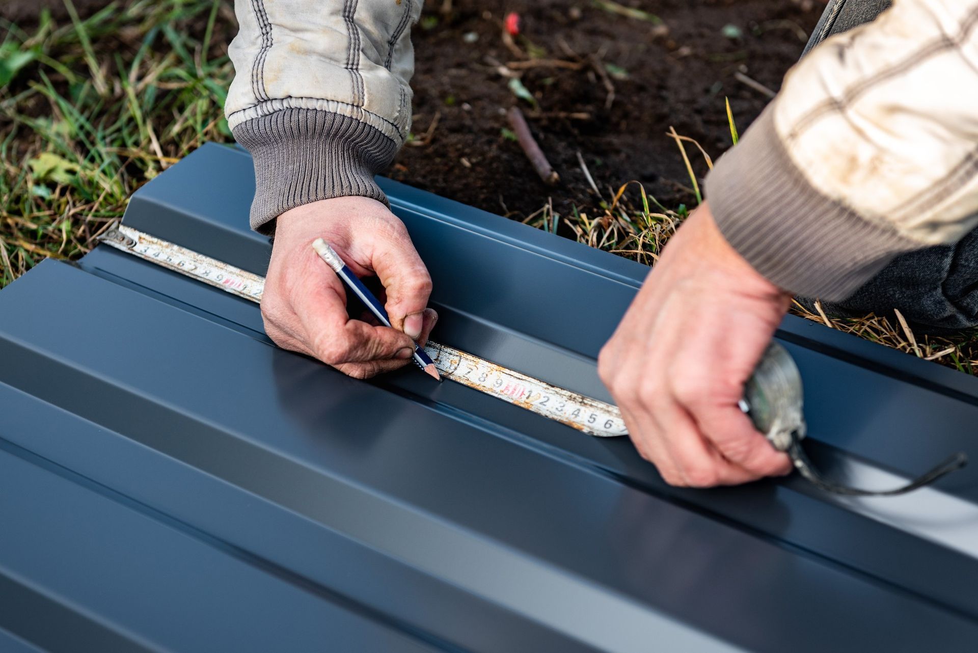 A man is measuring a piece of metal with a tape measure.