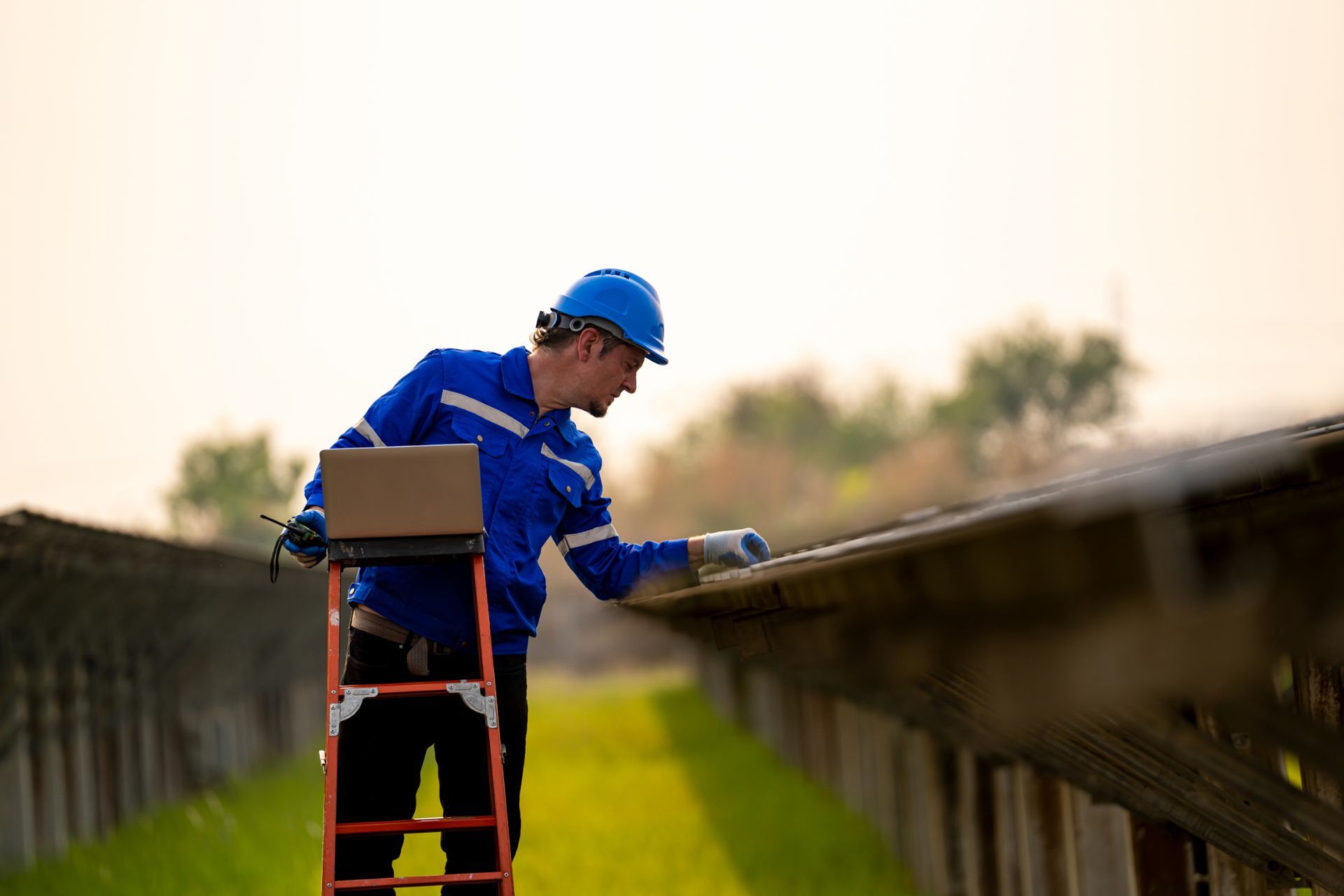 A man is standing on a ladder with a laptop.