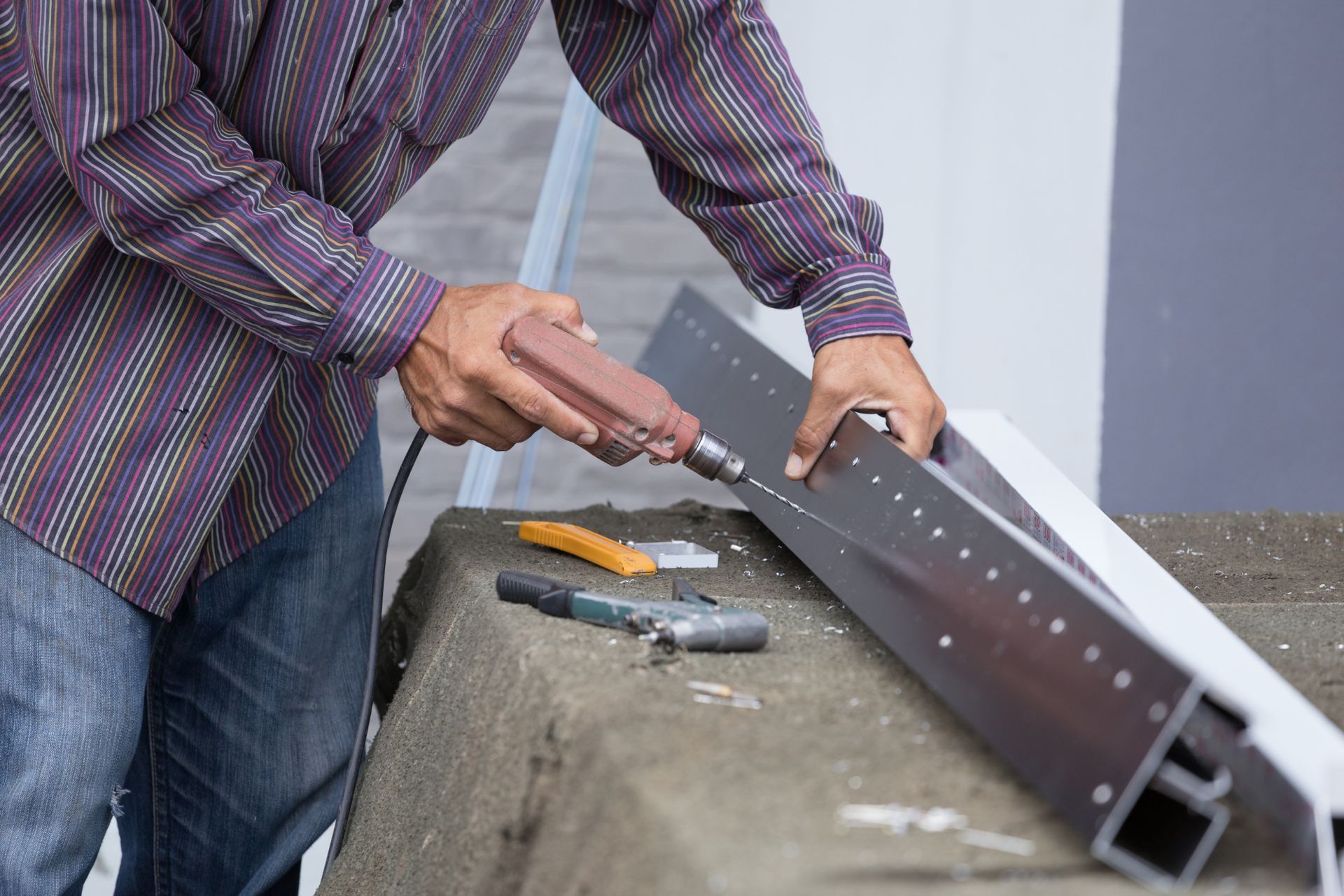 A man is using a drill to cut a piece of metal.