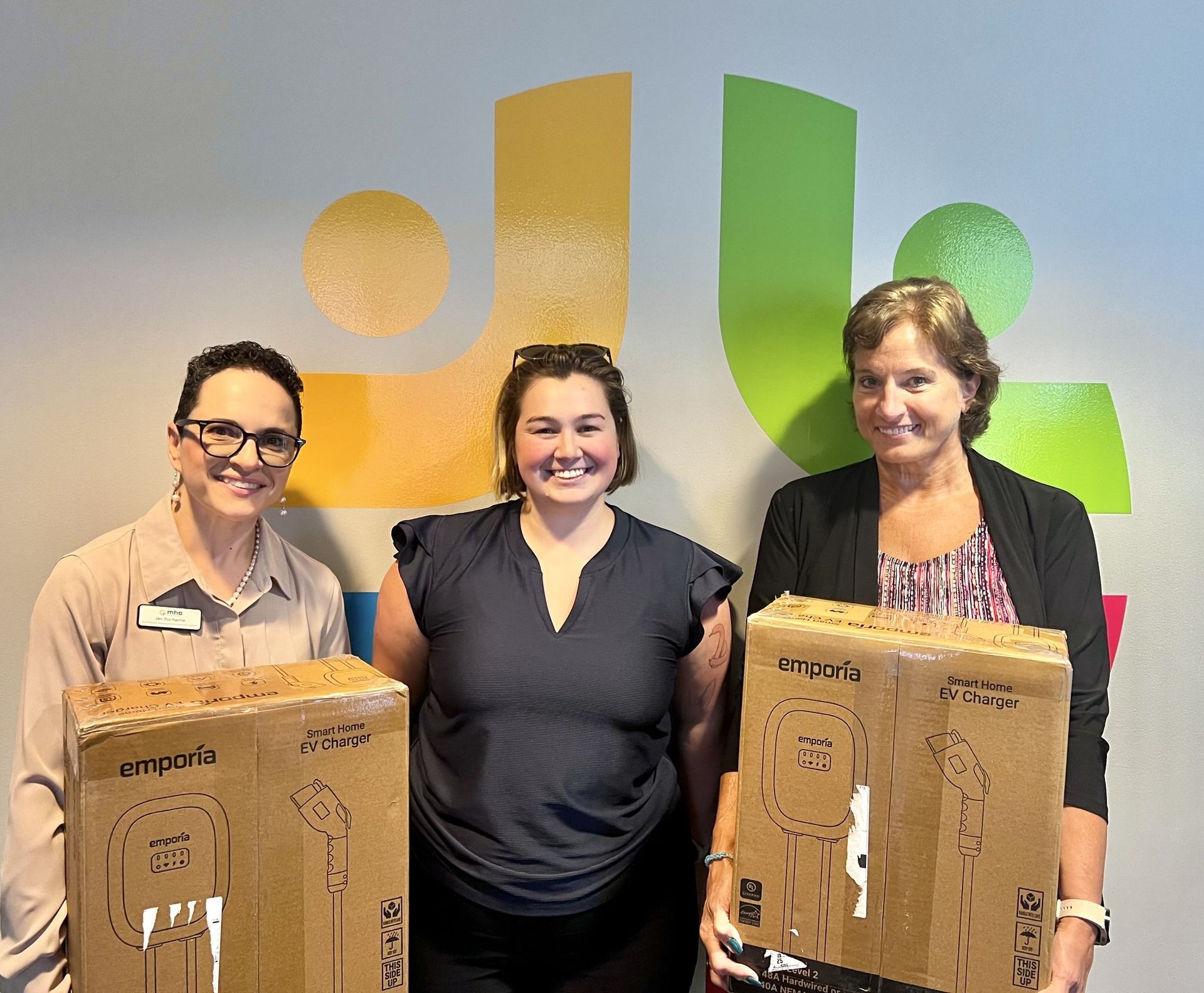 Three women are holding boxes in front of MHA logo.
