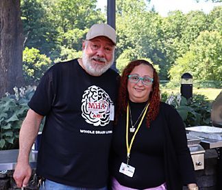 A man and a woman are posing for a picture in front of a grill.