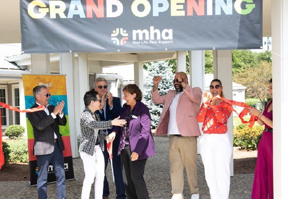 A group of people are standing in front of a sign that says grand opening.
