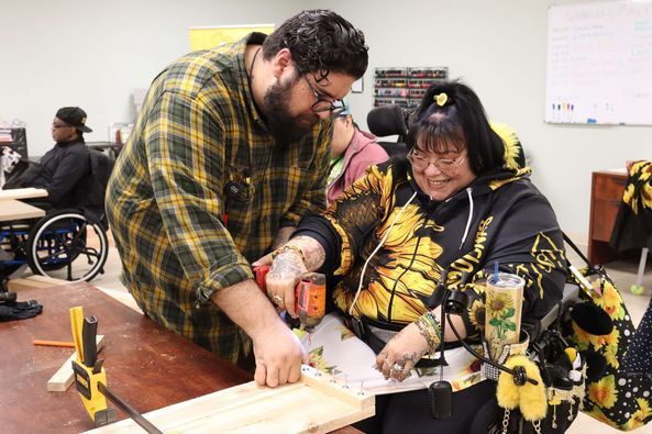 A man is helping a woman in a wheelchair with a drill.