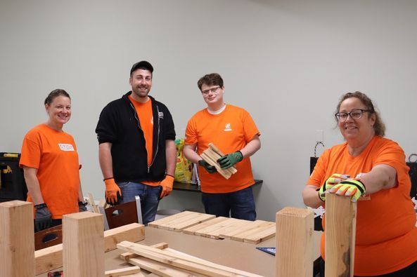 A group of people in orange shirts are working on a wooden table.