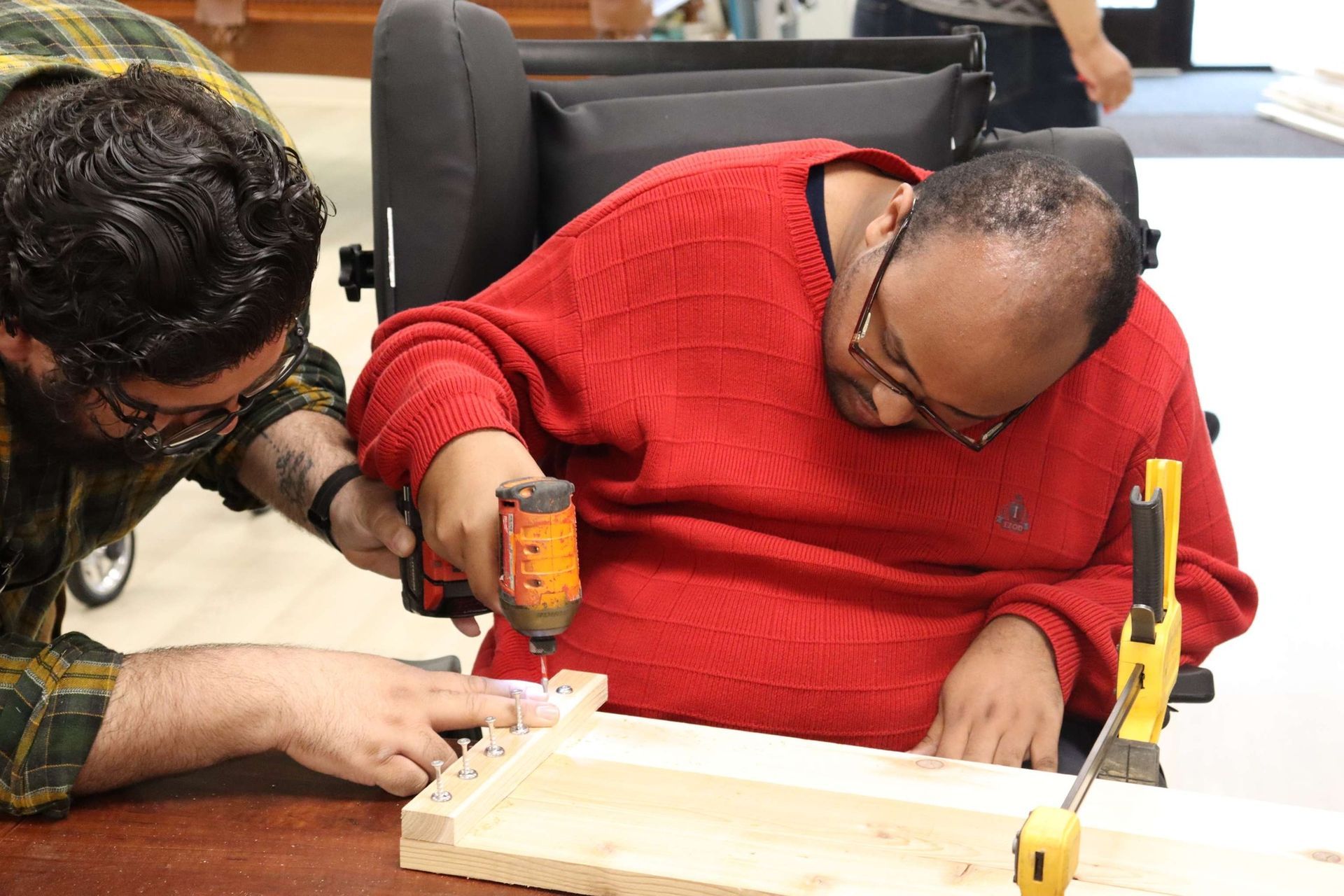 A man in a wheelchair is using a drill to drill a hole in a piece of wood.