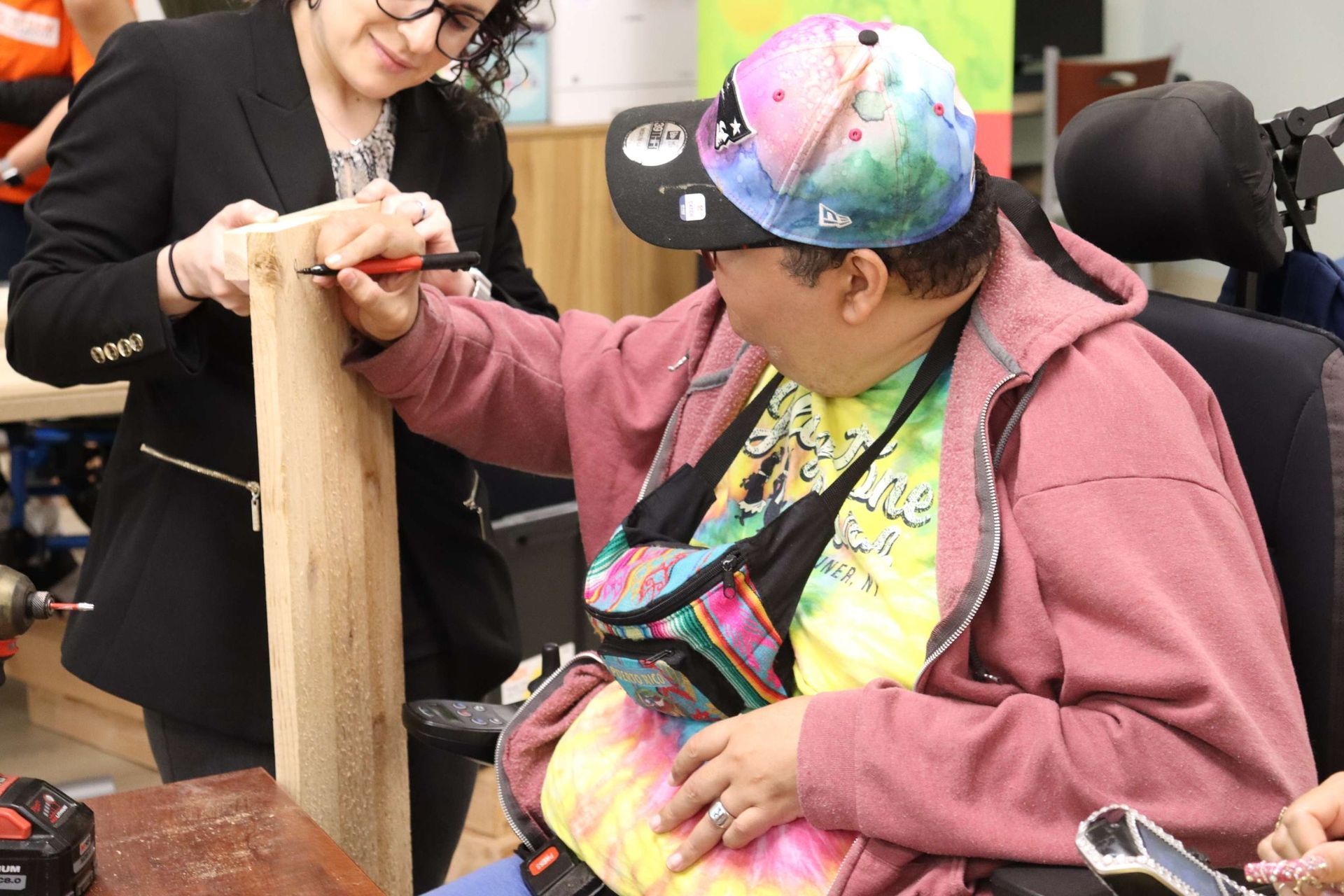 A woman is helping a man in a wheelchair with a piece of wood.