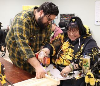 A man is helping a woman in a wheelchair with a drill.