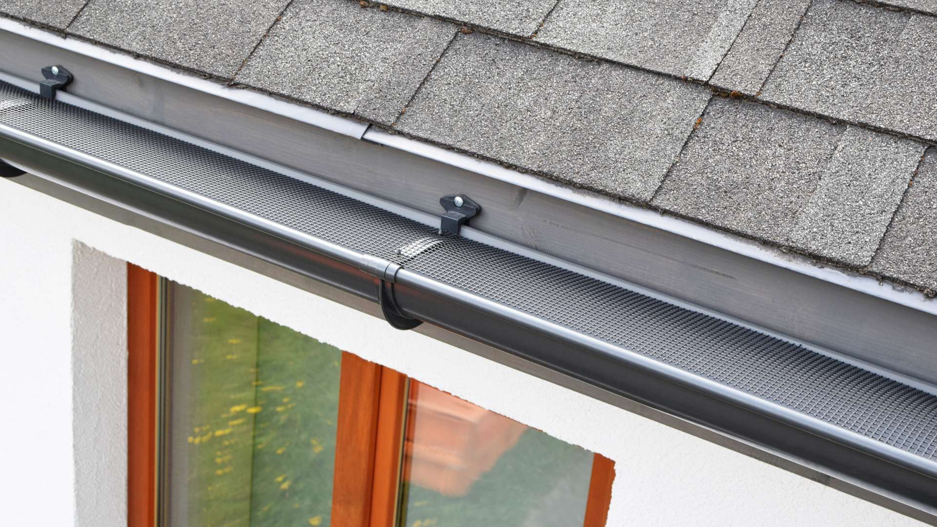 A close up of a gutter on a roof next to a window.