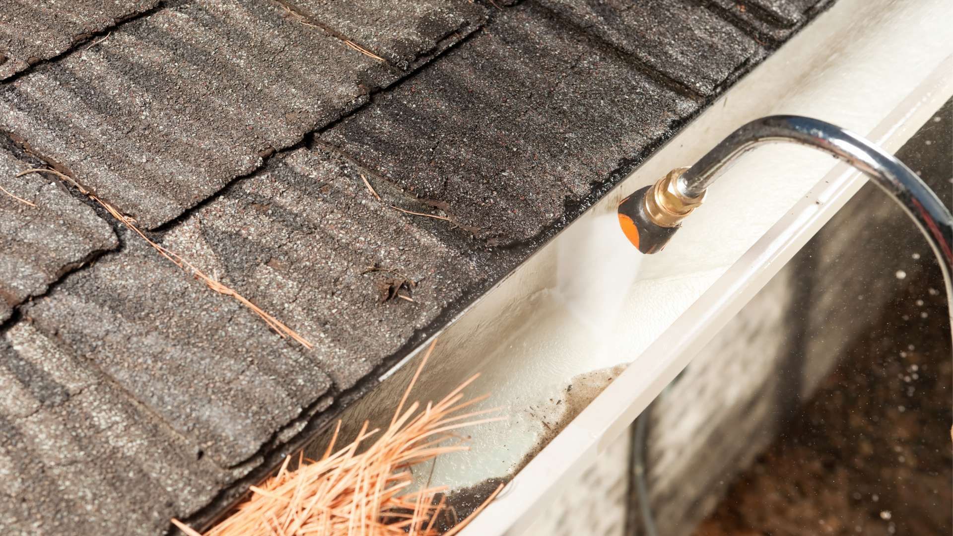 A gutter with a hose attached to it is being cleaned on a roof.