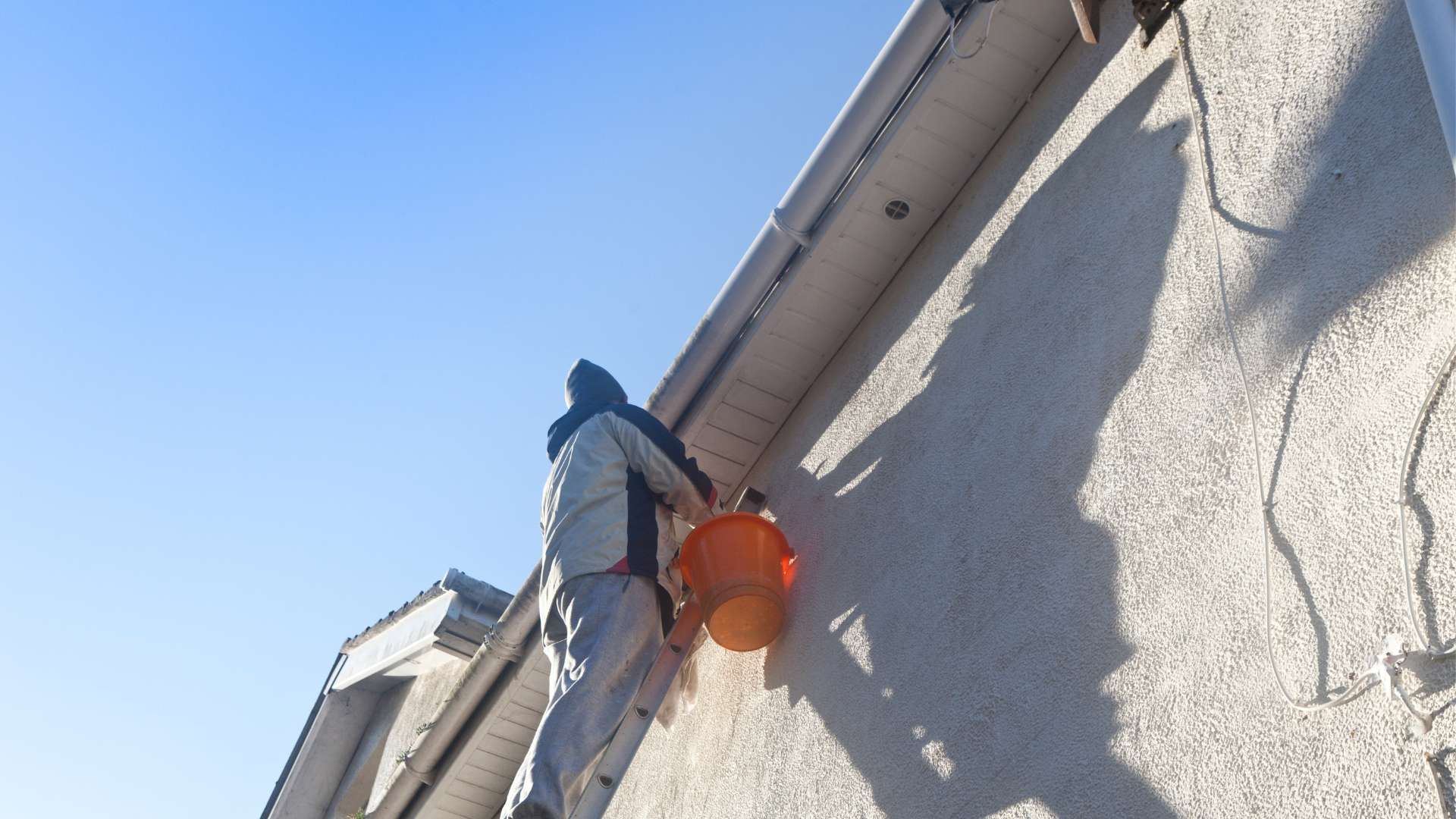 A man is standing on the side of a building holding an orange bucket.