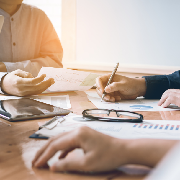 Close-up view of professionals collaborating over documents, charts, and a tablet on a wooden table.