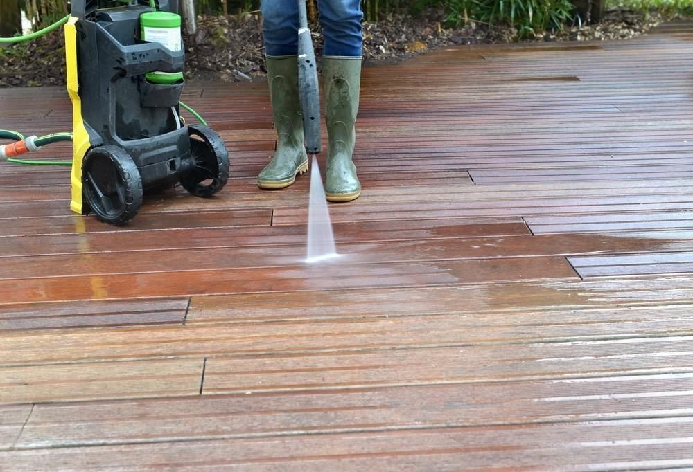 A person is cleaning a wooden deck with a high pressure washer.