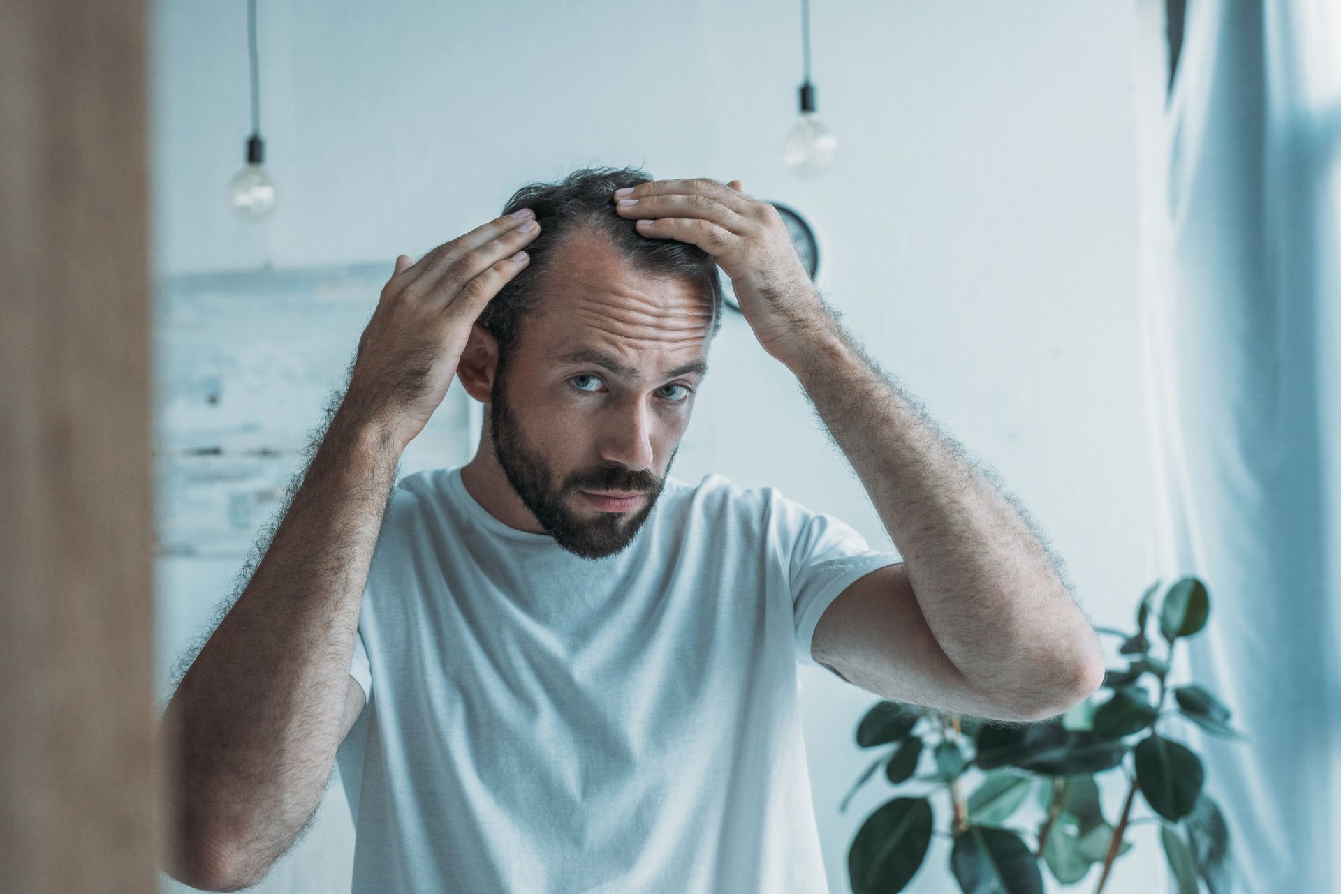 A man is looking at his hair in the mirror.