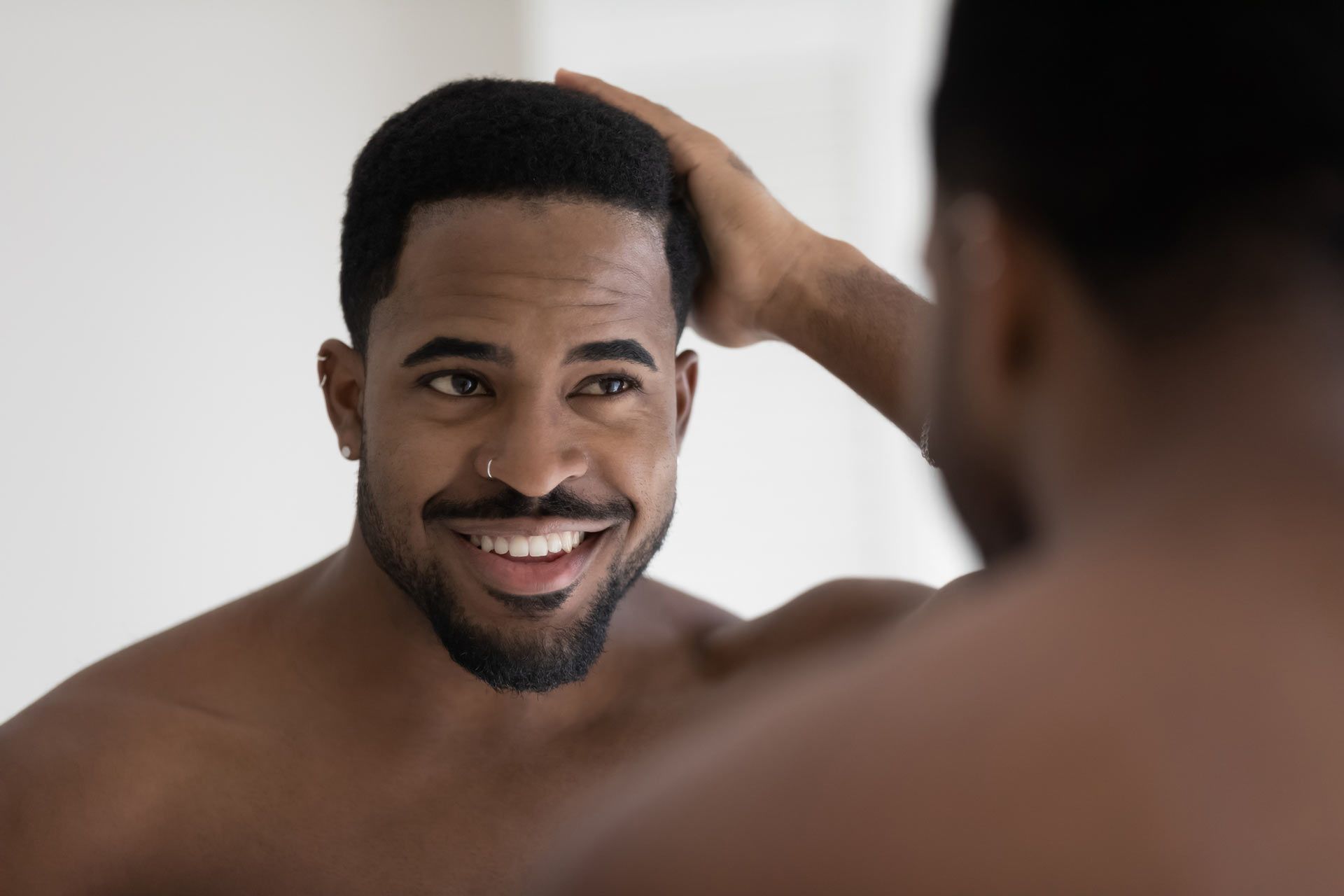 A shirtless man is smiling while looking at himself in the mirror.
