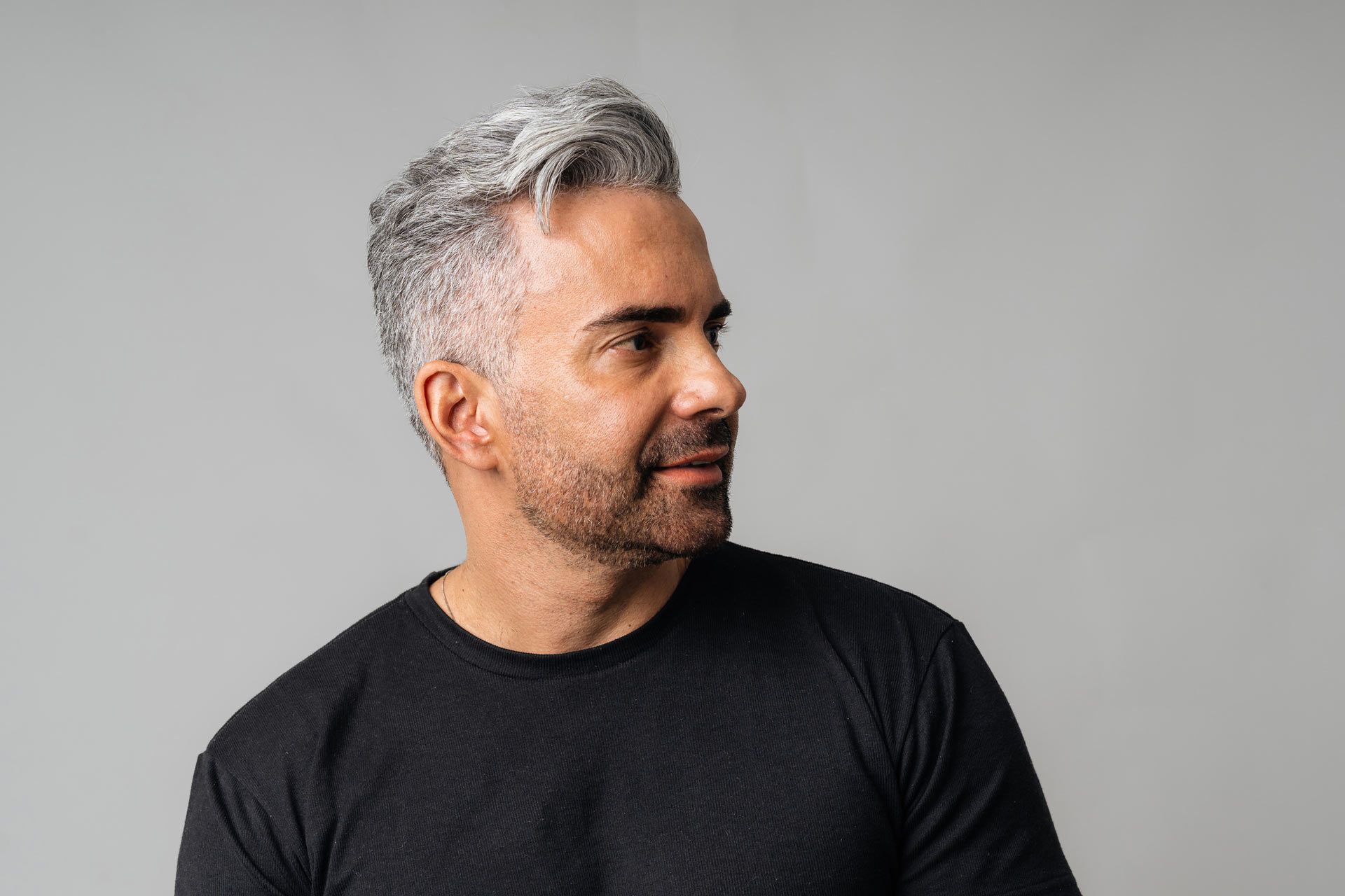 A man with gray hair and a beard is wearing a black shirt.