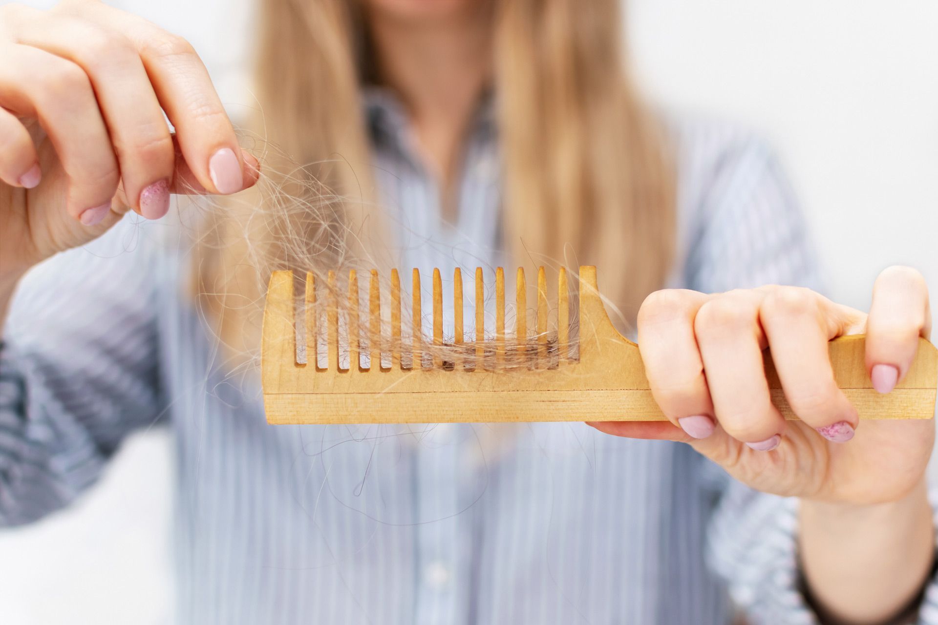 A woman is brushing her hair with a wooden comb.