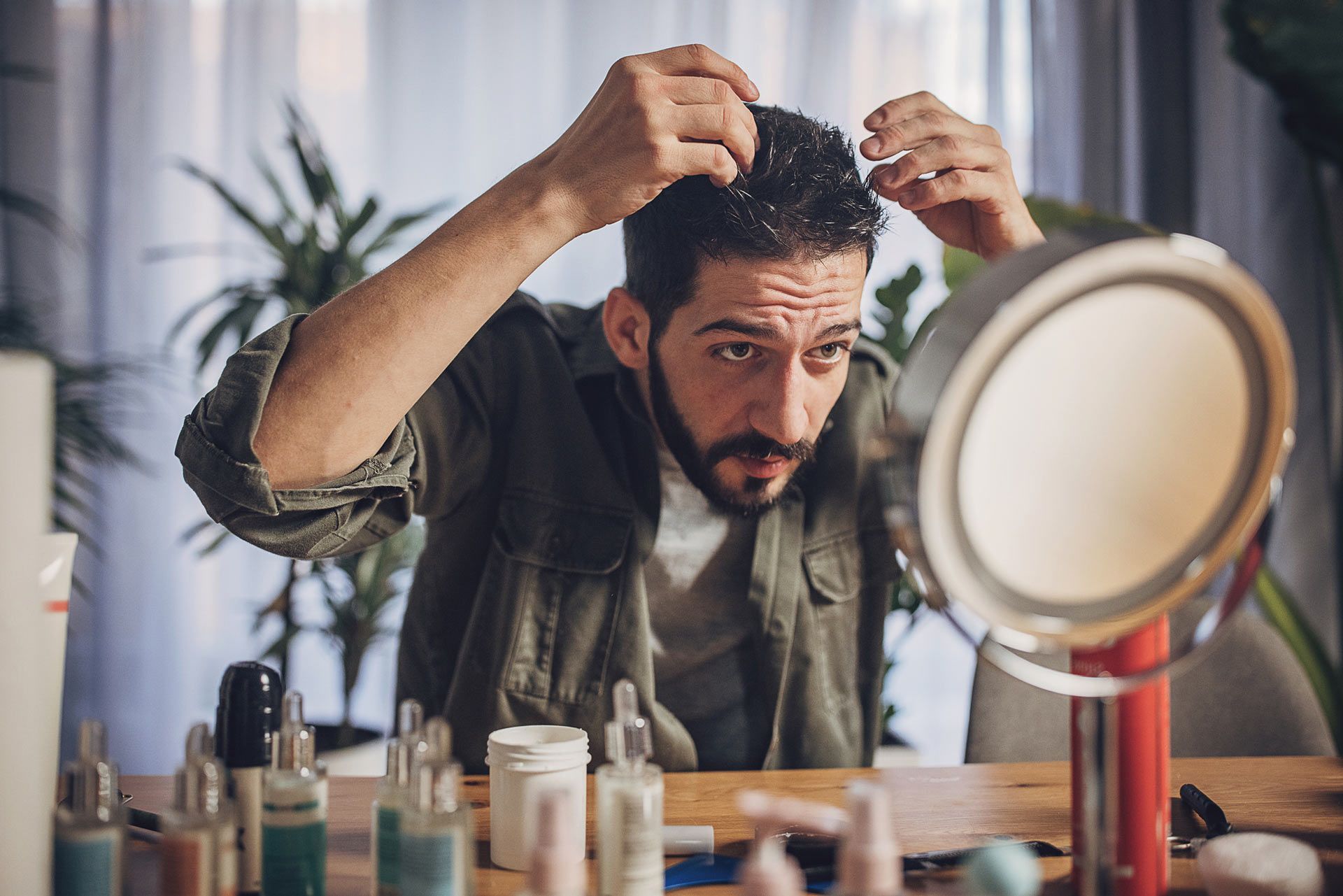 A man is looking at his hair in a mirror.