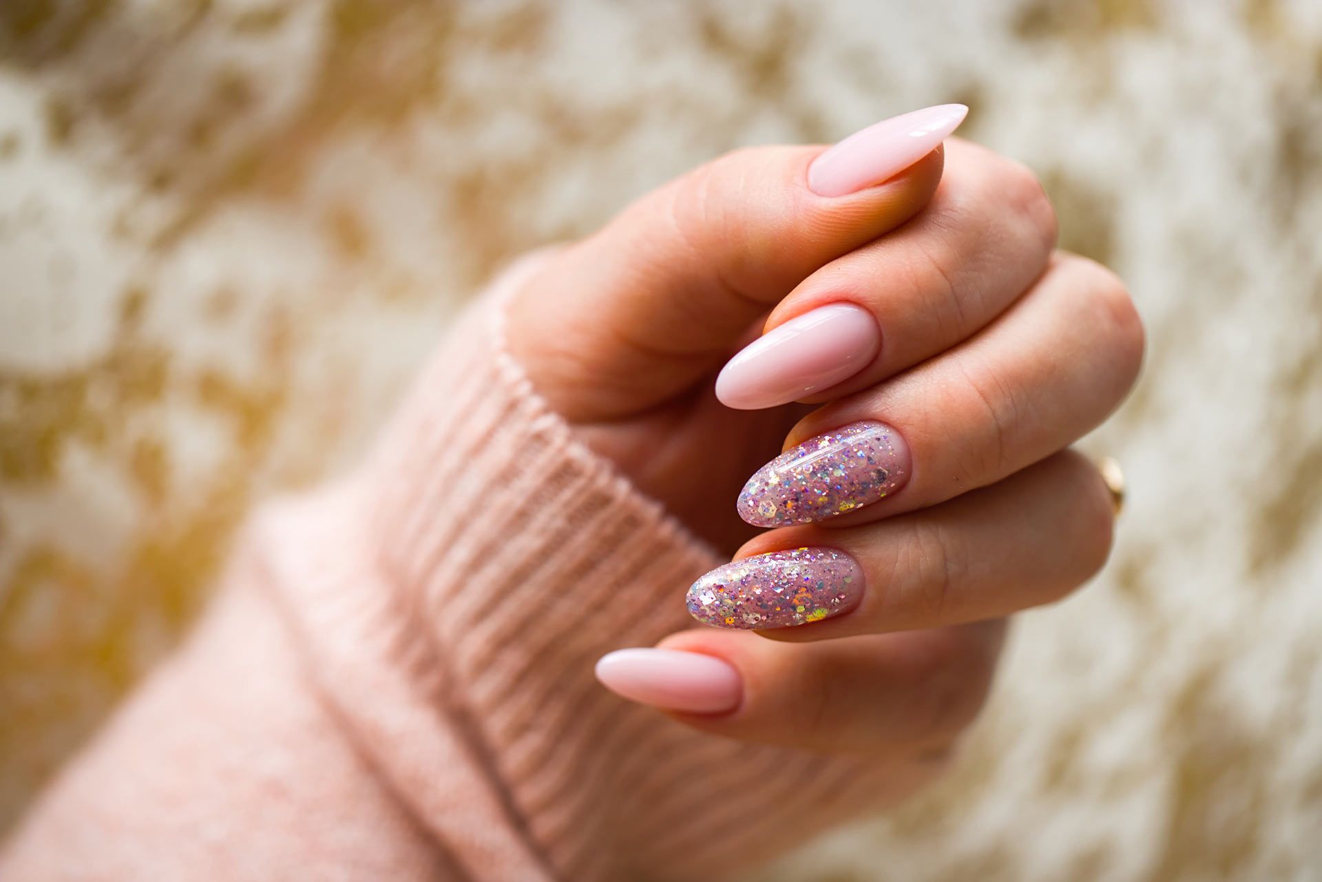 A close up of a woman 's hand with pink nails and a pink sweater.