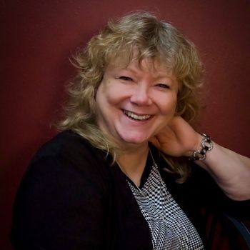 A woman is smiling and sitting in a chair with her hand on her chin.