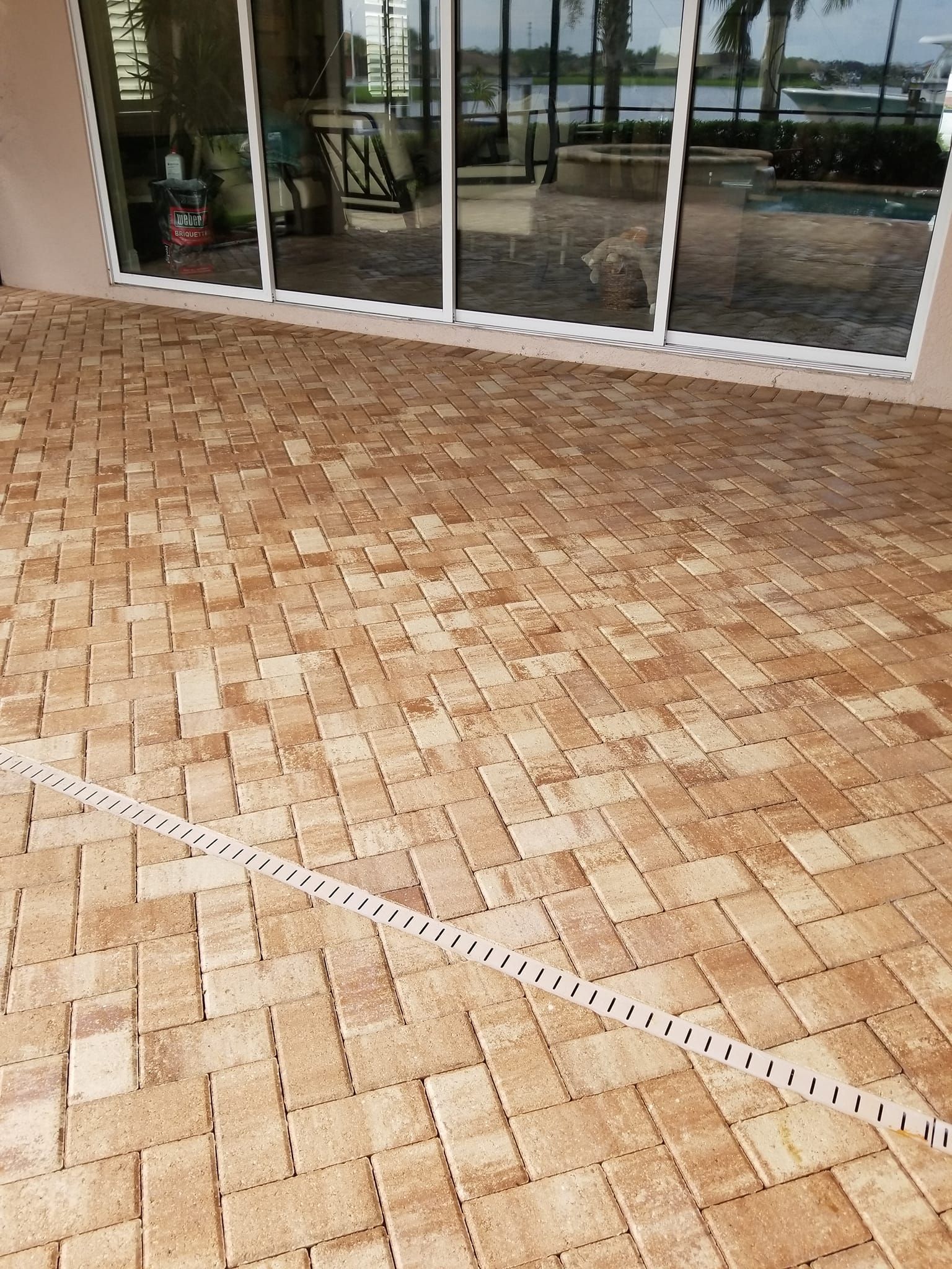 A ground-level view of a tan brick patio laid in a herringbone pattern with a long white measuring tape stretched across.