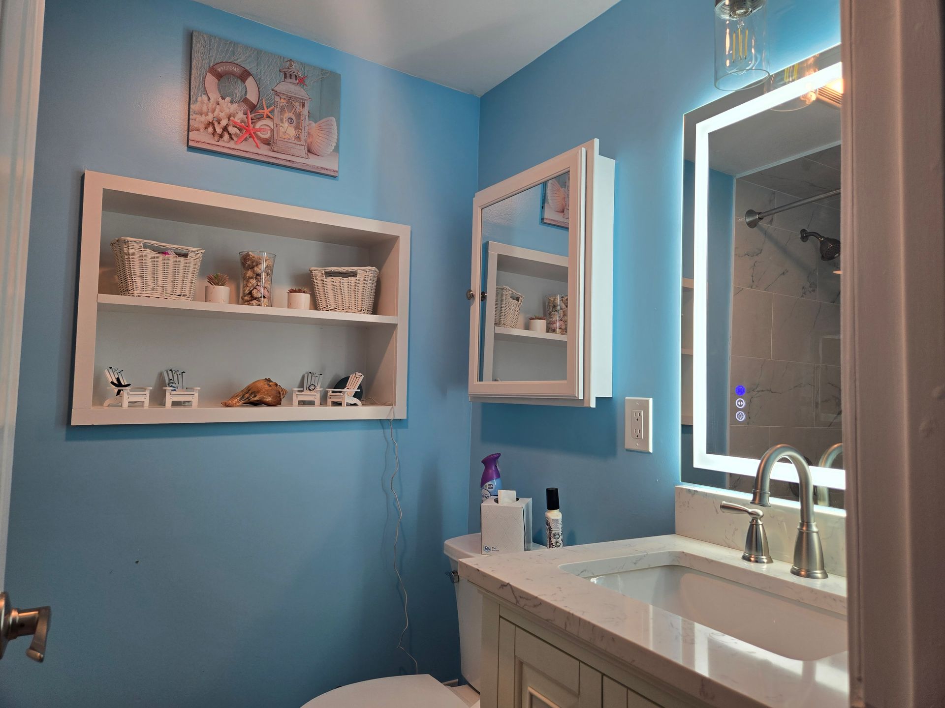 A bathroom with blue walls , a sink , toilet and mirror.