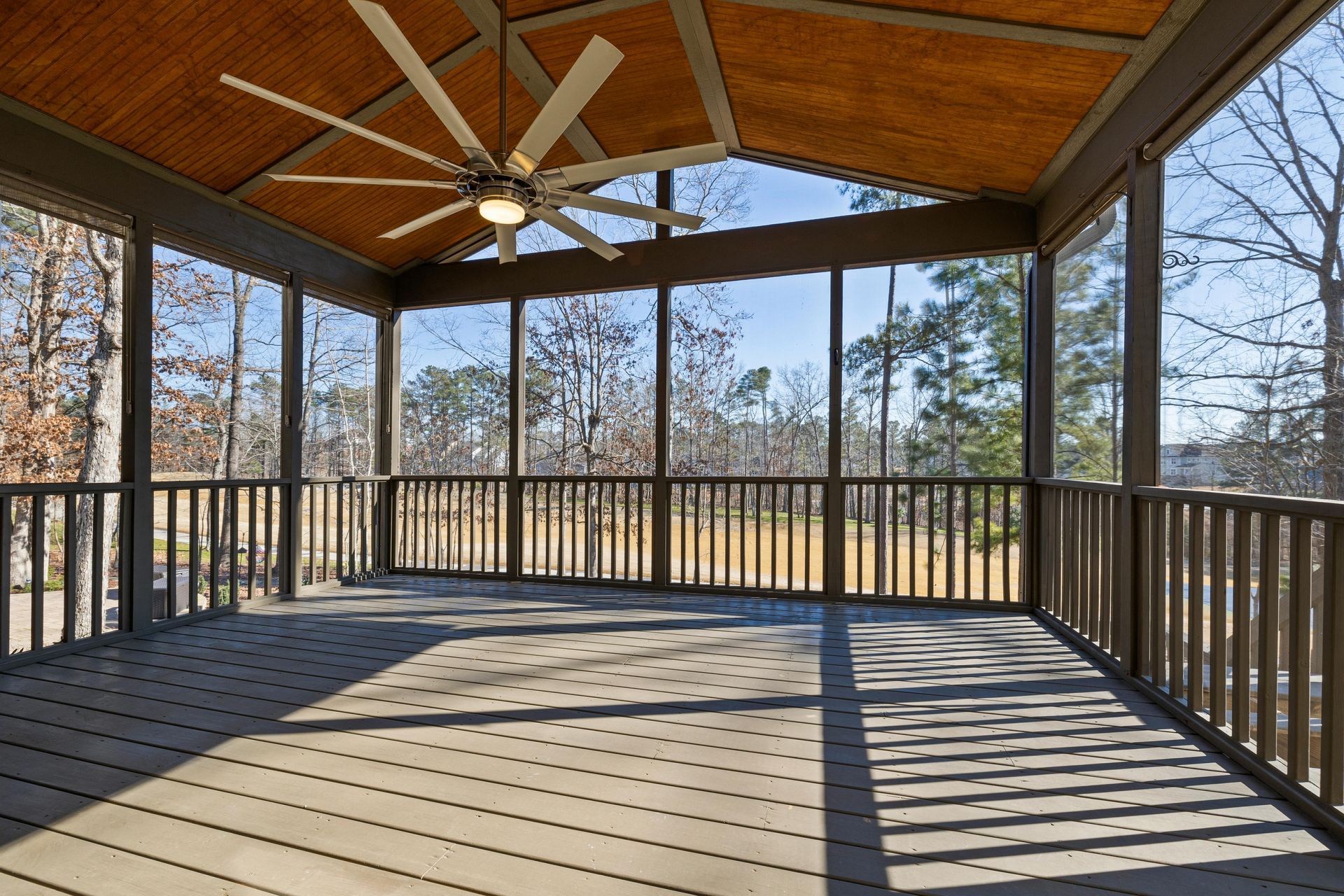 An empty screened in porch with a ceiling fan