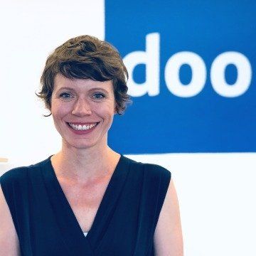 Eine Frau lächelt vor einem blauen Schild mit der Aufschrift „doo“