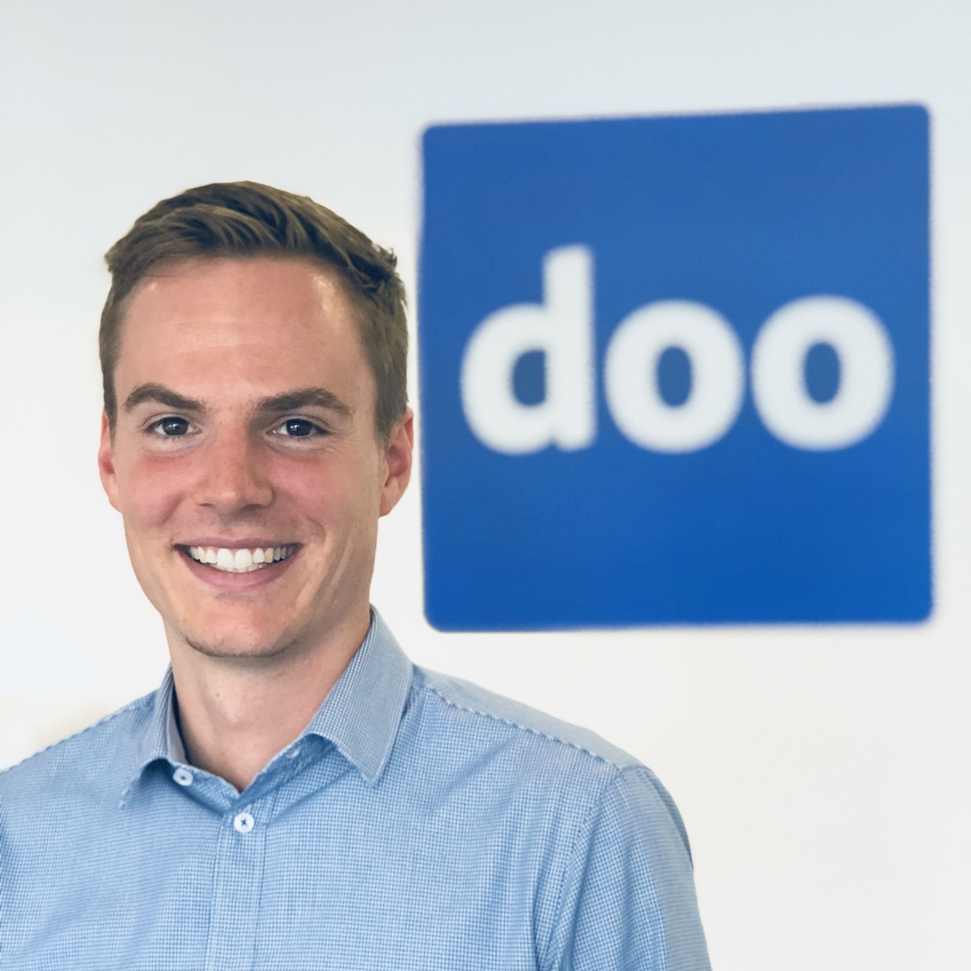 Ein Mann lächelt vor einem blauen Schild mit der Aufschrift „doo“